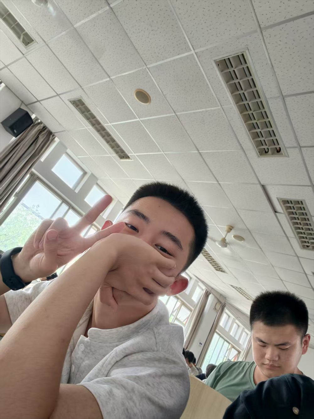 曹学艺在教室里对着镜头比手势自拍，笑得很开心