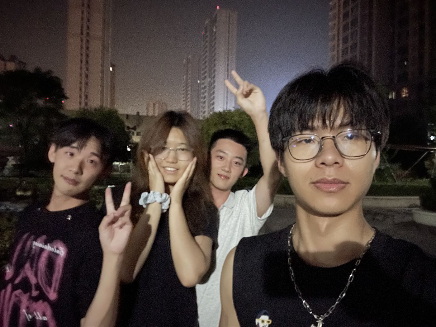 四个人在夜晚的小区里比着手势合影，背景是亮着灯的高楼
